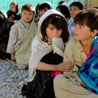 Copii din Afganistan, adunați într-un grup, stând pe jos.