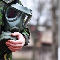 Soldat cu mască de gaz în mână, îmbrăcat în echipament de militar.