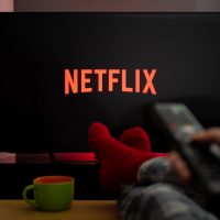 Persoana care se uita la Netflix cu o cana de ceai pe masa