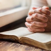 Persoana care se roagă cu mâinile împreunate pe Biblie