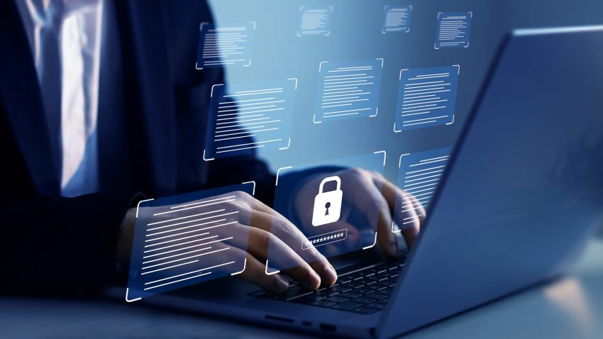 Bărbat în costum care scrie la un laptop, într-o încăpere întunecată.