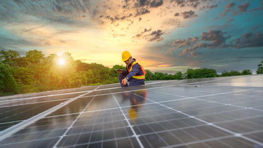 Un muncitor montează panouri fotovoltaice pe o casă.